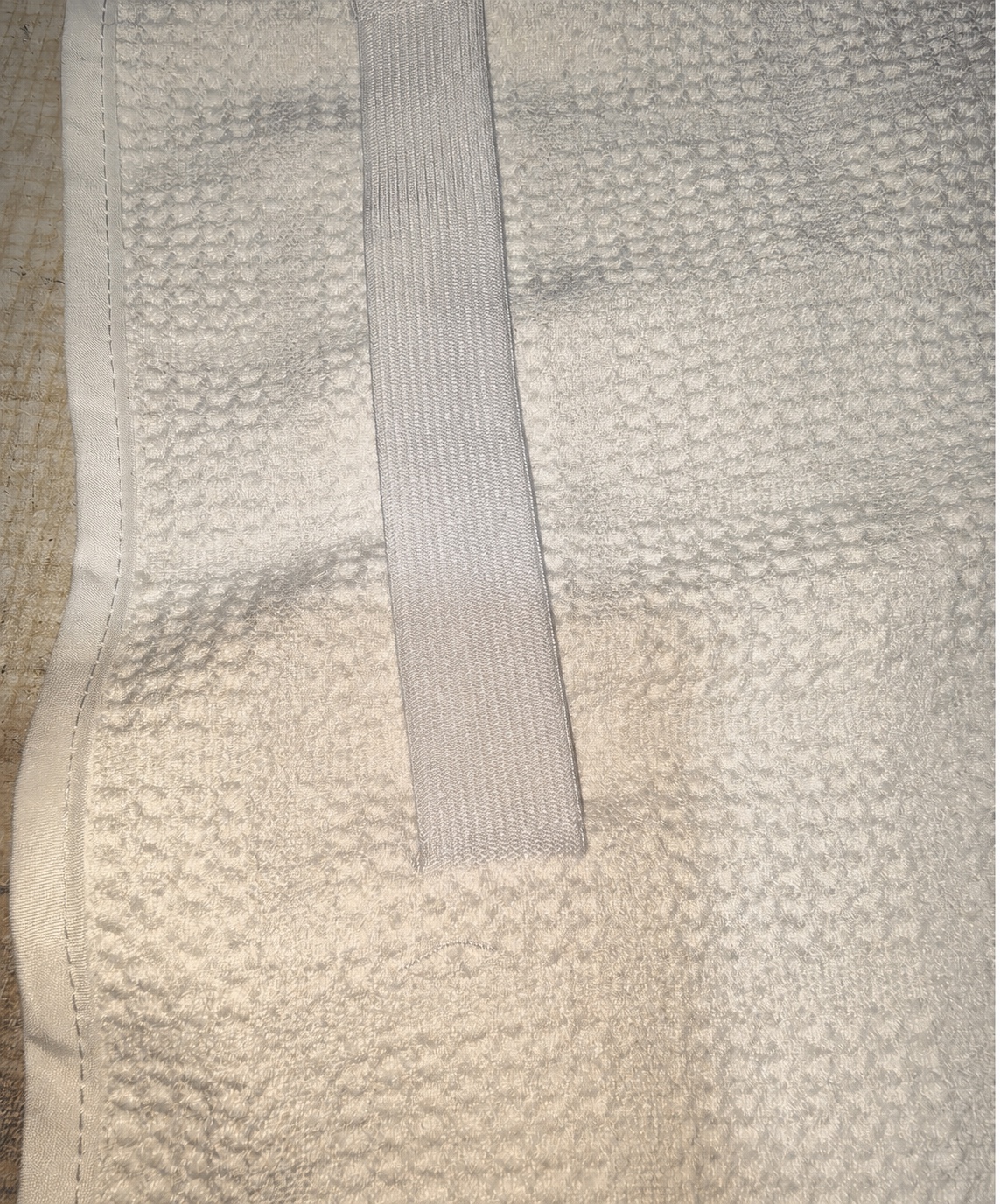Anonymized close-up of the wide elastic band and binding on a white waffle hair wrap