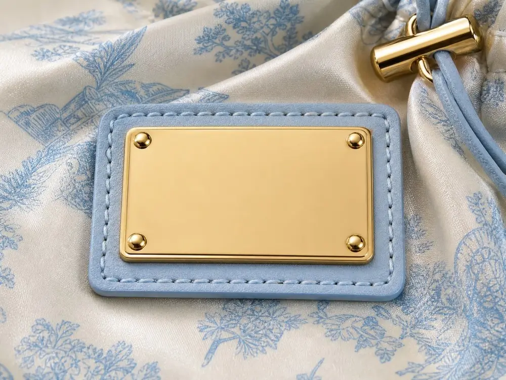 Blank gold-tone metal plaque fixed to a satin pouch with four corner studs